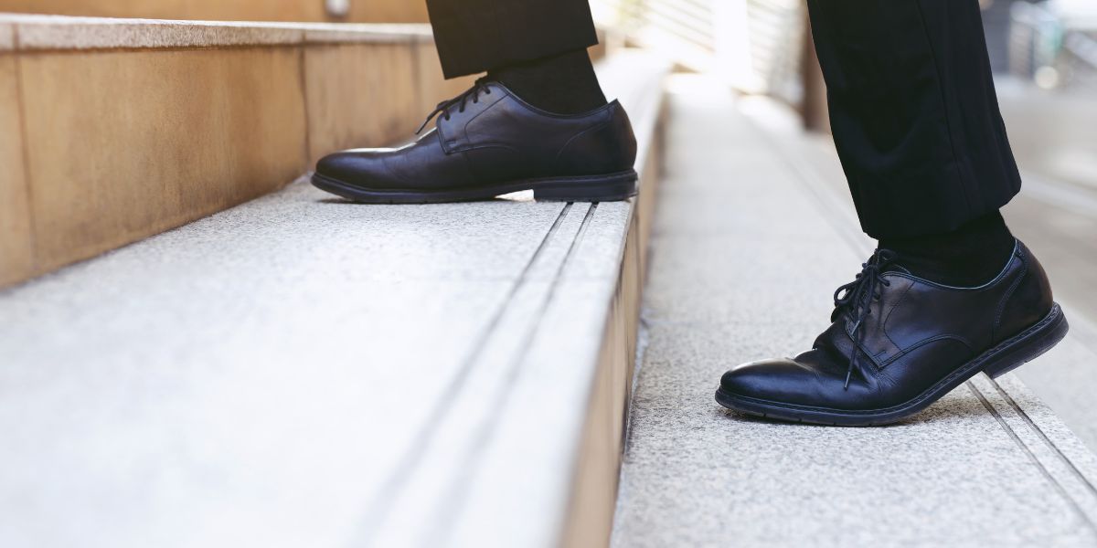 Man wearing suit shoes walking up a set of stairs.