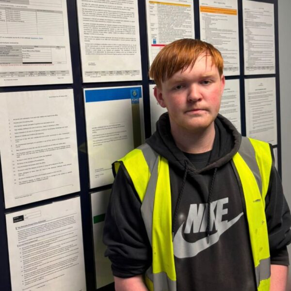 Young Man in a Hi Vis stop standing in font of a wall with various pieces of paper stuck to it.