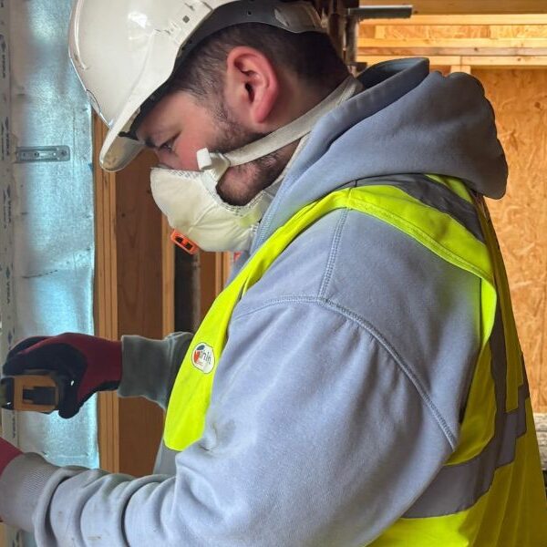 Young man wearing a PPE and holding a measuring tool while working on a construction site