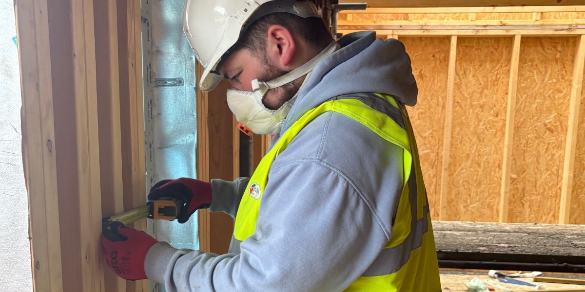 Young man wearing a PPE and holding a measuring tool while working on a construction site